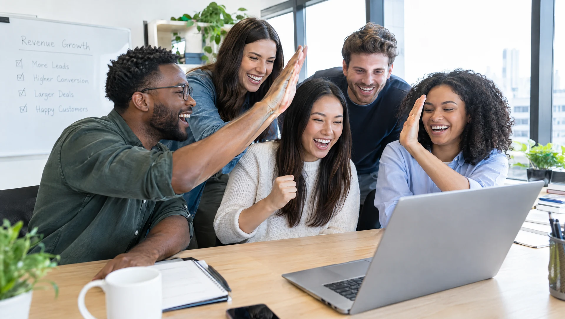 A revenue team of five cheering and high fiving around a laptop
