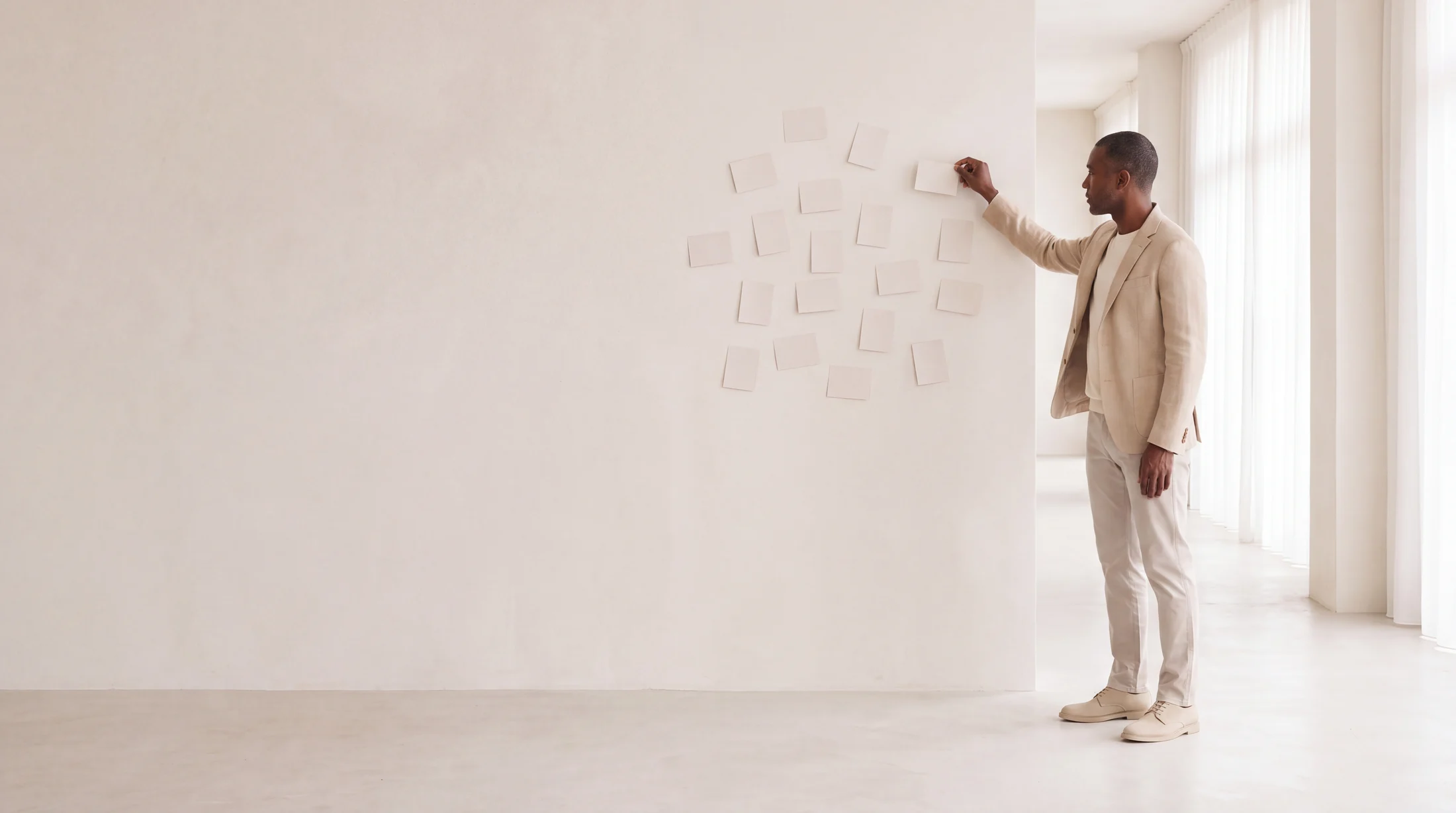 A man in a beige jacket pinning paper cards to a bright wall by hand, while two white graph8 agents stand idle to his right.